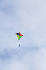 Multi coloured kite with tail ribbon flying against a cloudy sky