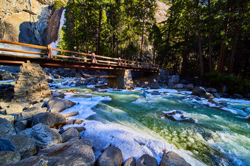 Bridge by Yosemite Lower Falls crossing over dangerous frosty and slushy cold river during early spring