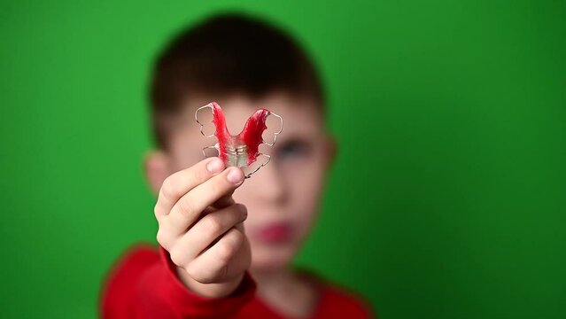 Plate for aligning teeth, a boy on a green background holding a plate, a dental plate in his hands.