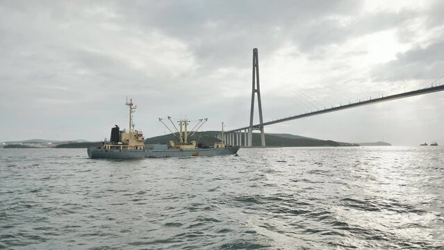 Vladivostok Bridge. View from a moving ferry at sunset with a ship in the background.