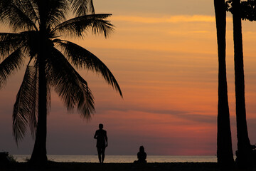 Two people, under coconut palms, watch the beautiful sunset on Thailand's Andaman coast
