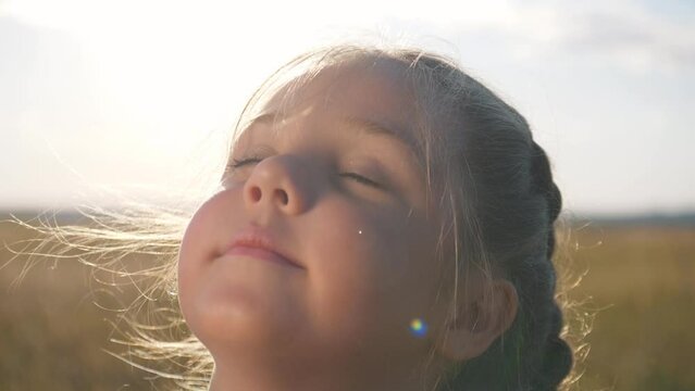 Happy baby. Cute free teenage girl dreaming with her eyes closed. Baby's face of little girl in rays of sun outdoors. Emotions of freedom of girl dreaming with closed eyes. Positive emotions on face