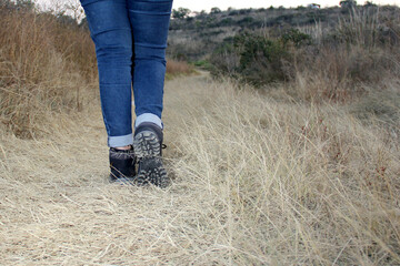 Naklejka na ściany i meble Legs with denim pants and black hiking boots in the middle of the field walk, pose, play, explore, discover and live in freedom 