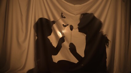 Unrecognizable woman and boy telling spooky stories using shadow play and paper bats and pumpkins....