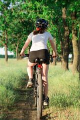 Obraz premium Rear view of a cyclist. A girl rides a bicycle along a forest path.