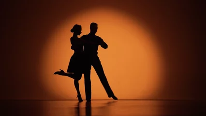 Fotobehang Dansschool Een paar dansers naderen elkaar en beginnen Argentijnse tango te dansen. Elementen van latin ballroomdans in studio met oranje bruine achtergrond. Donkere silhouetten. Klaar voor slow motion, 4K met 59,94 fps.