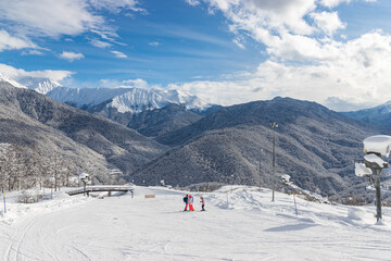 Fototapeta na wymiar KRASNAYA POLYANA, RUSSIA - JANUARY 29, 2022: Skiers at the ski slope in mountain village in Krasnaya Polyana ski resort. Snowy mountains of Caucasus on background.