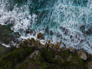 Overhead view of The bluish ocean waves crashing against the rocks on the beach produce white ripples and foam in tropical beach