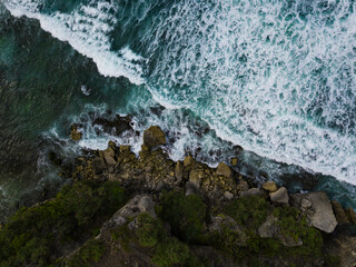Overhead view of The bluish ocean waves crashing against the rocks on the beach produce white ripples and foam in tropical beach