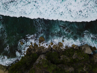 Overhead view of The bluish ocean waves crashing against the rocks on the beach produce white ripples and foam in tropical beach