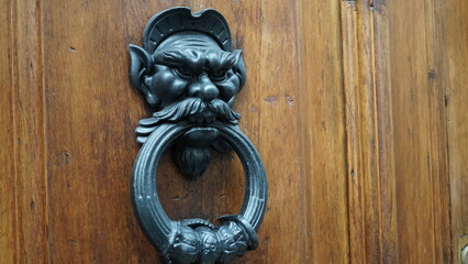 Door knocker of wood, in decorative metal with ring and mask of a mustachioed demon of a city...