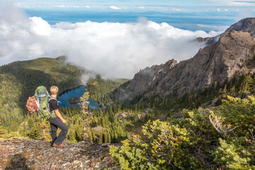 Hiker overlooking mountain lake and forest in summer with sea fog encroaching