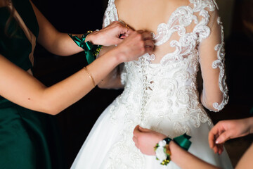 Obraz na płótnie Canvas Bridesmaid's hands help the bride fasten the buttons on the back of a beautiful white wedding lace dress, the concept of preparing in the morning for the wedding day