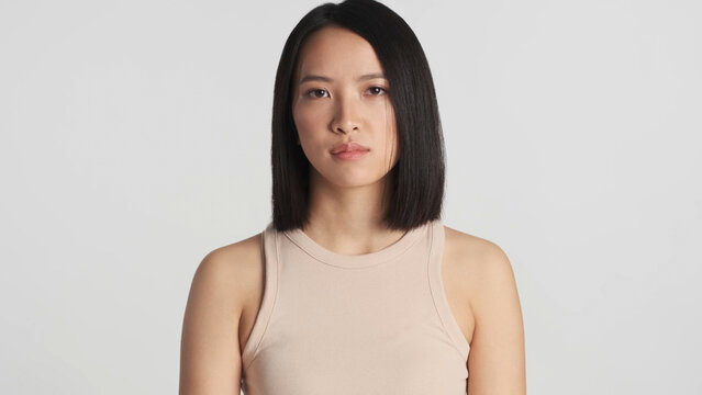 Young beautiful Asian woman intently looking at camera standing over white background. Female posing isolated