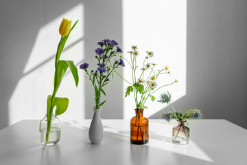 flowers in a vase. different flowers on a white table in sunlight.