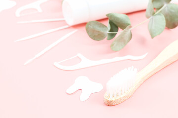 Bamboo toothbrush, dental floss, toothpicks and a tube of toothpaste on a soft pink