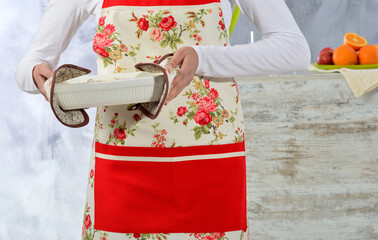 Cooking and homemade food concept. Young woman chef in apron standing and holding fresh cooked dinner meal in hands