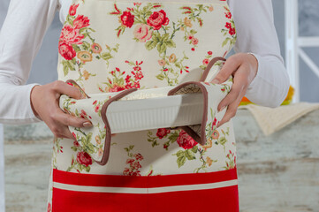 Cooking and homemade food concept. Young woman chef in apron standing and holding fresh cooked dinner meal in hands
