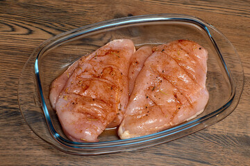 raw chicken fillet marinated in a glass dish on a dark wooden table
