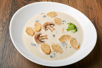 mushroom soup with champignons, croutons and broccoli in a white plate on a dark wooden background