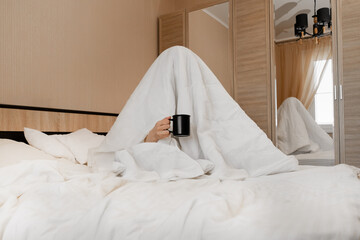 A person under a blanket with a cup of coffee can not cheer up, does not want to get out of bed and...