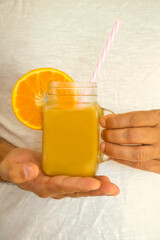 Male hands holding a glass with natural juice from fresh oranges on white background.