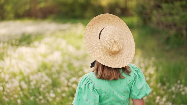 Back view of happy free woman in vintage dress and straw hat running through bloom lawn countryside. Carefree lifestyle, stylish romantic unrecognizable lady. Retro fashionista like from novel