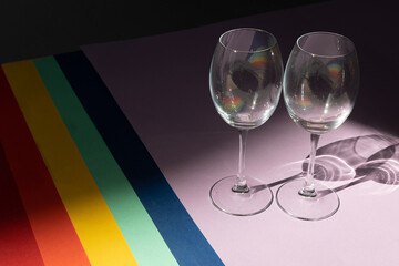 Top view on colored paper backgrounds laid out in the LGBT Pride Flag with two glasses. LGBT flag colors. Celebration concept.