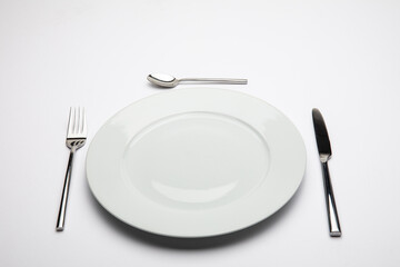 Empty white plate with spoon, knife and fork on white background