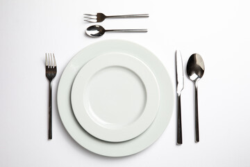 Empty white plate with spoon, knife and fork on white background