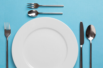 Empty white plate with spoon, knife and fork on blue background