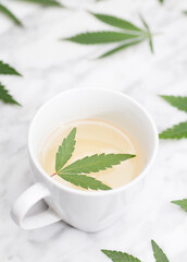 white mug with marijuana infusion with green leaf inside on marble table with leaves. top view.