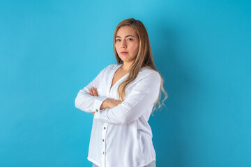 Beautiful attractive young business woman posing seriously, in white shirt and grey pants. Isolated over blue background.