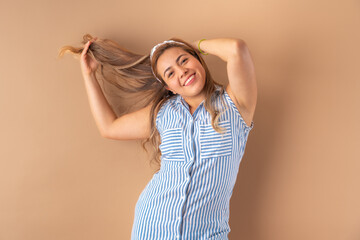 Beautiful attractive young woman posing happily, in striped blue dress. Isolated over brown background.