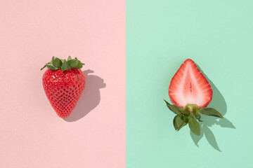One whole and one sliced strawberry on a pastel pink and tiffany green background with sharp...