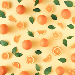 Creative summer pattern made of oranges and green leaves on pastel yellow background. Fruit minimal concept. Flat lay.