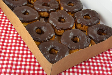 Open box of donuts with chocolate icing on red and white check tablecloth