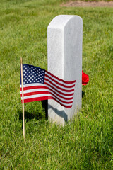 Close up view of a single military gravestone decorated with an American flag and a simple bouquet of flowers