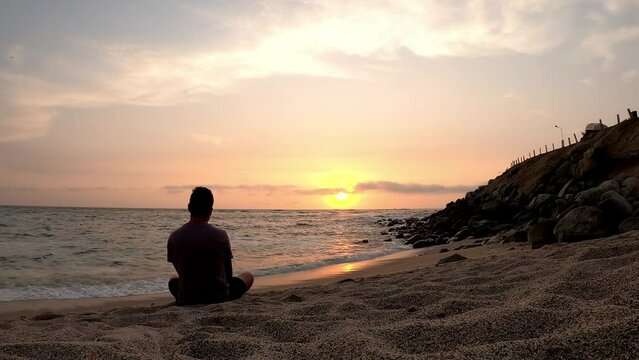 quick camera of a man sitting on the sand looking longingly at the sea with the waves and the sun at sunset, timelapse in 4k