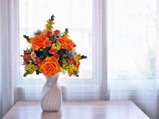 Orange roses artificial flowers bouquet in vase on table, copy space for text or writing ,pretty background or wallpaper ,mother's day ,still life ,women's day festive background ,colorful elegant 