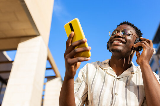 Black young man relaxing outdoors listening to music using phone and headphones. Copy space.