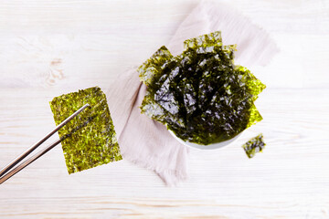 Chopsticks with a piece of crispy dried seaweed. Nori, Japanese edible seaweed in a plate. A healthy snack. © Viktoriya