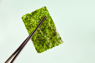 Chopsticks hold a piece of crispy dried seaweed. Nori, Japanese edible seaweed. Healthy snack. Close-up