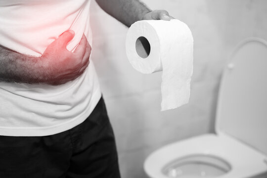 Man suffers from diarrhea hand hold tissue paper roll in front of toilet bowl. constipation in bathroom. Treatment stomach pain and Hygiene, health care