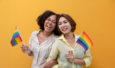 Couple of same sex marriage holding LGBTQ rainbow flag for pride month to promote equality and differences of homosexual and discrimination concept isolated on yellow background