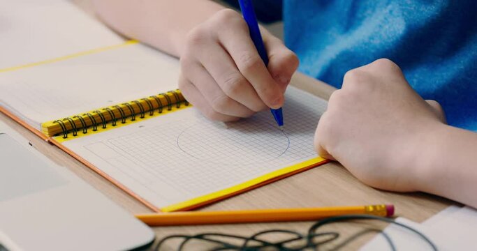 Shot of young boy's hands drawing circles, diagrams on paper in notebook, child creates notes for school, learns.