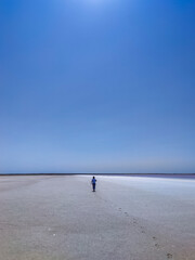 Fototapeta na wymiar A woman walks on dried salt on the shore of a lake looking into the distance. An unusual natural phenomenon is a lake with red salt water on the site of an extinct mud volcano