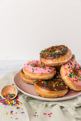 There are several sprinkle donuts on a pink plate. The donuts are chocolate and strawberry. There are sprinkles on the side.