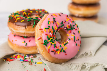Strawberry and chocolate sprinkled donuts stacked up. In the for ground there are two donuts stacked with a strawberry donut leaning against them. In the background is a stack of donuts. 