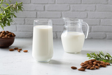 A glass of almond milk, next to a carafe, almonds and green twigs.